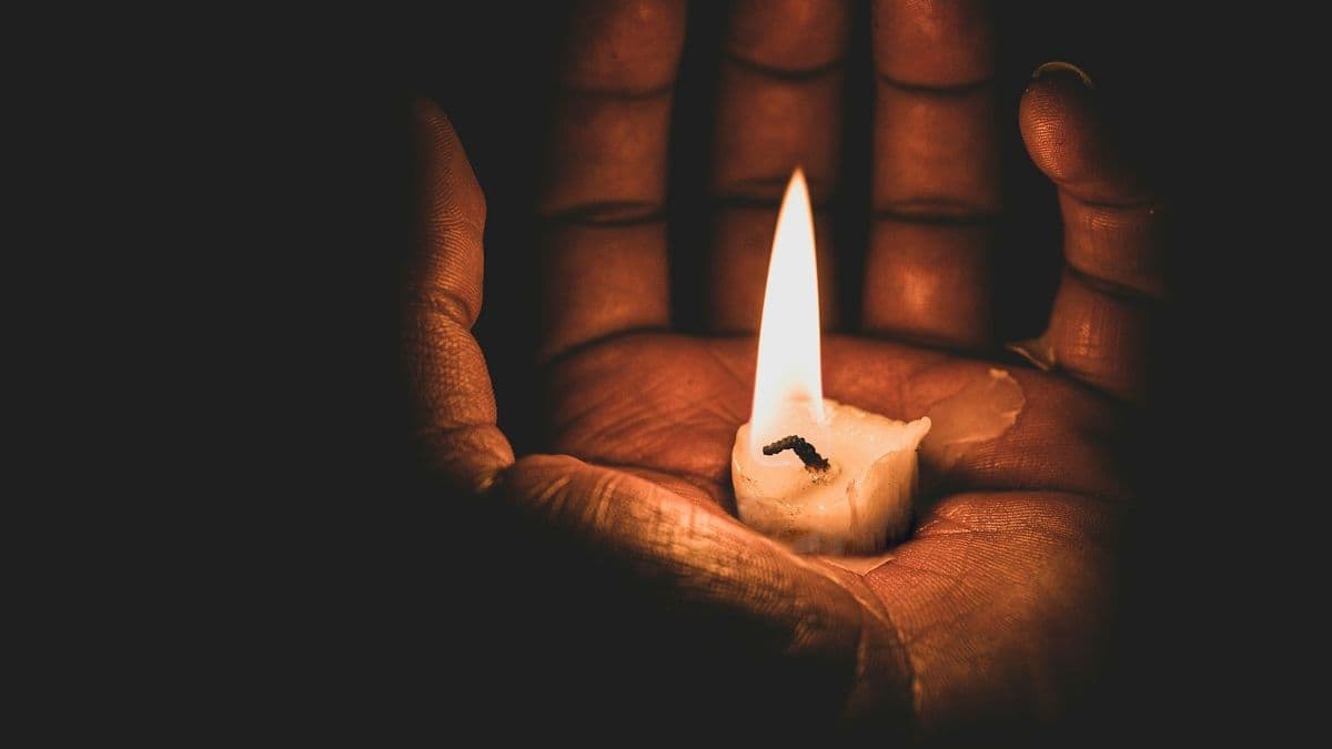 A single lit candle held in an open hand against a dark background